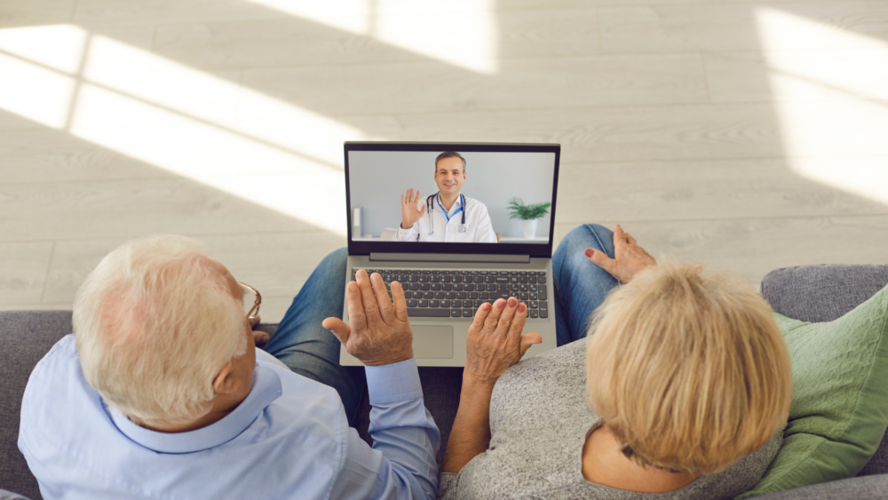 retired couple communicating remotely with their doctor via video on their laptop screen