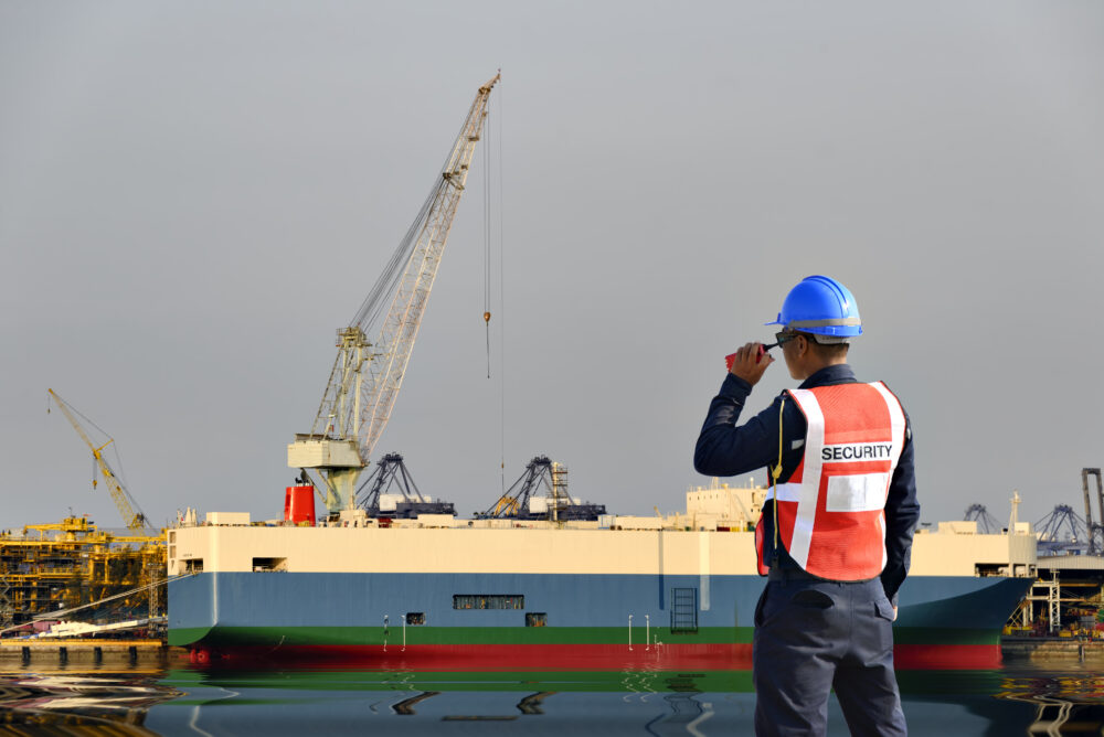 A cargo ship in a port with a man wearing a helmet and a "safety" vest.
